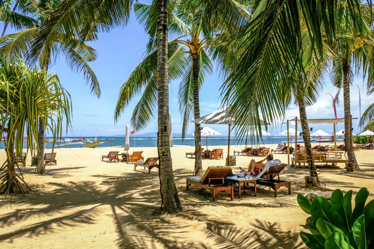 Sanur beachfront with palm trees, loungers and traditional boats by the water